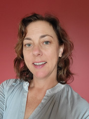 Headshot of middle aged woman with blue eyes and wavy, mid-length hair against red background