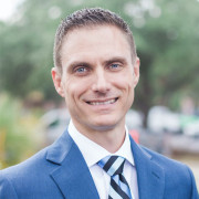 Headshot of a 40-something year old man with short light brown hair and blue eyes, dressed in a blue suit