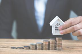 Coin stacks with a model house on wooden table