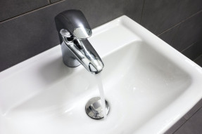 running water from bathroom faucet black tiles in background