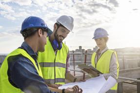 Construction workers and architect looking at blueprints on construction site