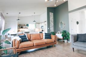 A teal and white living room with ash wood floor, light tan leather couch, and grey love seat.