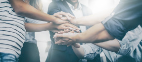 Close up view of young business people putting their hands together.