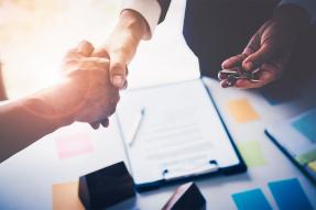 Business handshake over papers on a clipboard