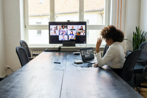 Rear view of a businesswoman having a meeting with team over a video conference in office board room.