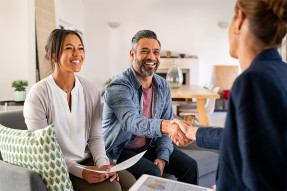 Clients on couch in home shaking hands with agent