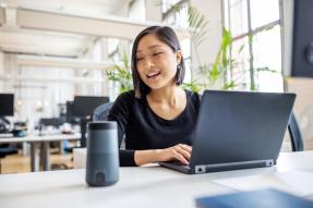 Female professional working on laptop and talking into a speaker.