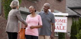 Real Estate Agent shaking hands with older couple outside house for sale