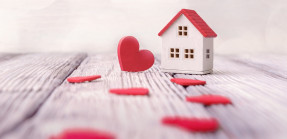 Toy house and red hearts on light defocused background