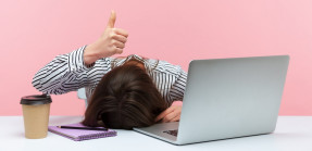 Woman with head down at desk holding up a thumbs up