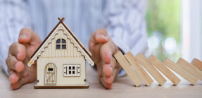 Hand between house and falling dominoes