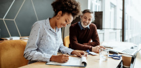 Woman signing a piece of paper with man in background