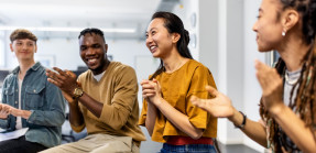 Group of business people sitting in a circle clapping hands in meeting