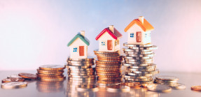 Miniature colorful houses on stacks of coins