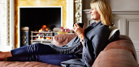 woman sitting on her sofa drinking tea while wrapped in a blanket