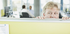 Businessman peering over cubicle wall in office