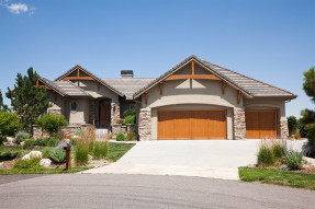 Gray stone and wood house with a landscaped yard on a sunny day