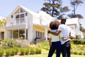 Weekend fun at home together. Rear view of a mixed race couple standing in the garden, embracing and looking at the house