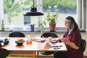 Older woman sitting at a dining room table with a credit card and a laptop