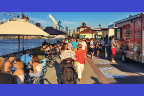 People strolling and sitting at tables along the Hoboken Waterfront walkway, NJ