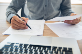 Person in front of a laptop holding a pen and reviewing papers