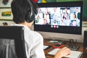 Person wearing headphones and watching a conference call on a computer