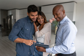 Real estate agent and clients standing in kitchen looking at tablet