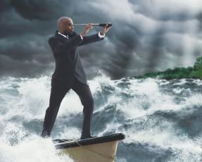 Businessman standing on a boat with a telescope in choppy waters at sea