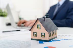 Toy house on desk with laptop and pen and papers