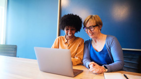 Two businesswomen with laptop, blue backdrop