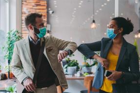 Two professionals wearing masks and bumping elbows