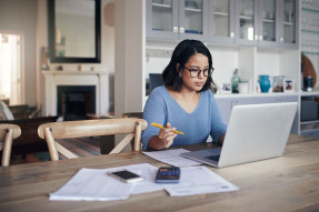 Woman sitting at kitchen table concentrating on laptop screen