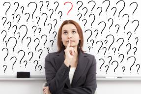 A Woman in business attire, looking thoughtful in front of a white board of question marks