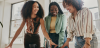 Three black women smiling as they look down at a table at paperwork, teamwork