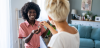 An smiling, Black woman with an afro is handed the keys to a new home by a white woman with short blonde hair