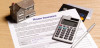 A picture of a home insurance document, a calculator, and a house miniature on a table.