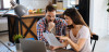 A man and a woman at a table review insurance documents in front of a laptop.