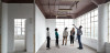 A group of people touring an office building point to a ceiling with exposed pipes.