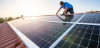 A man installs solar panels atop a house's roof