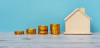 A set of stacked coins from left to right growing taller leading to a house miniature.