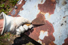 Gloved hand scraping lead based paint from a door