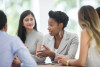 A group of multi-ethnic adults sit around a boardroom table having a business meeting