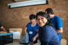 Smiling volunteer in foreground more volunteers and brick wall in background