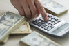 Stacks of U.S. currency and person using calculator